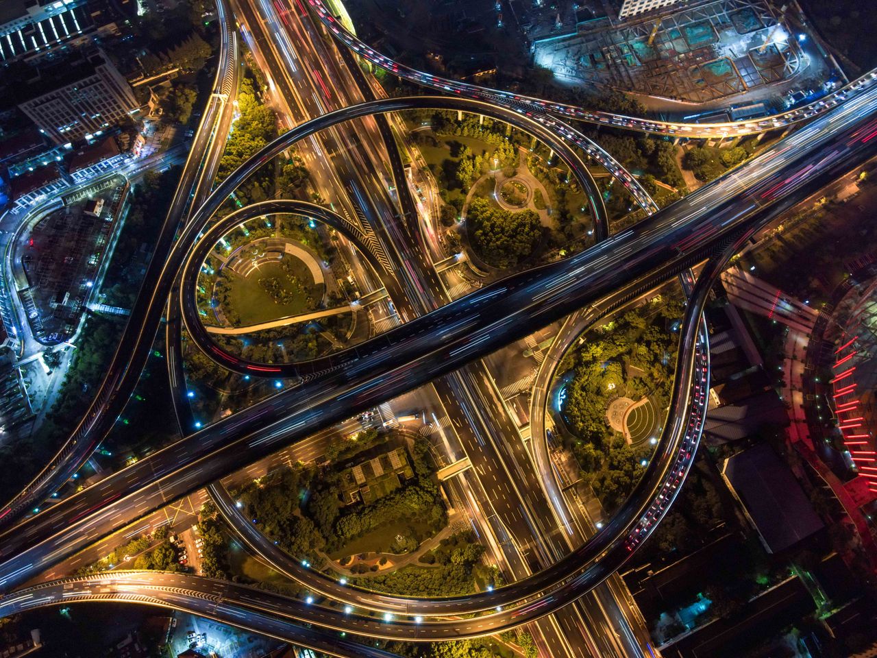 hero-img-01 Stunning aerial view of intricate city highways and roundabouts illuminated at night.