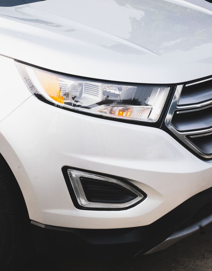 gallery-4 Detailed view of a white SUV's headlight, showcasing sleek automotive design.