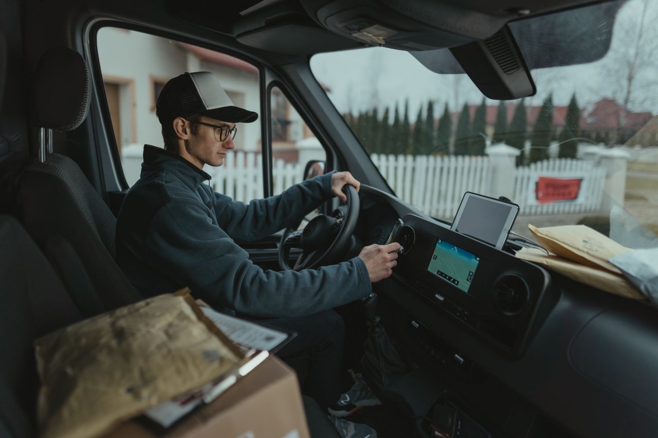 hero-img-02 Courier driving van with packages, using GPS for efficient delivery route.