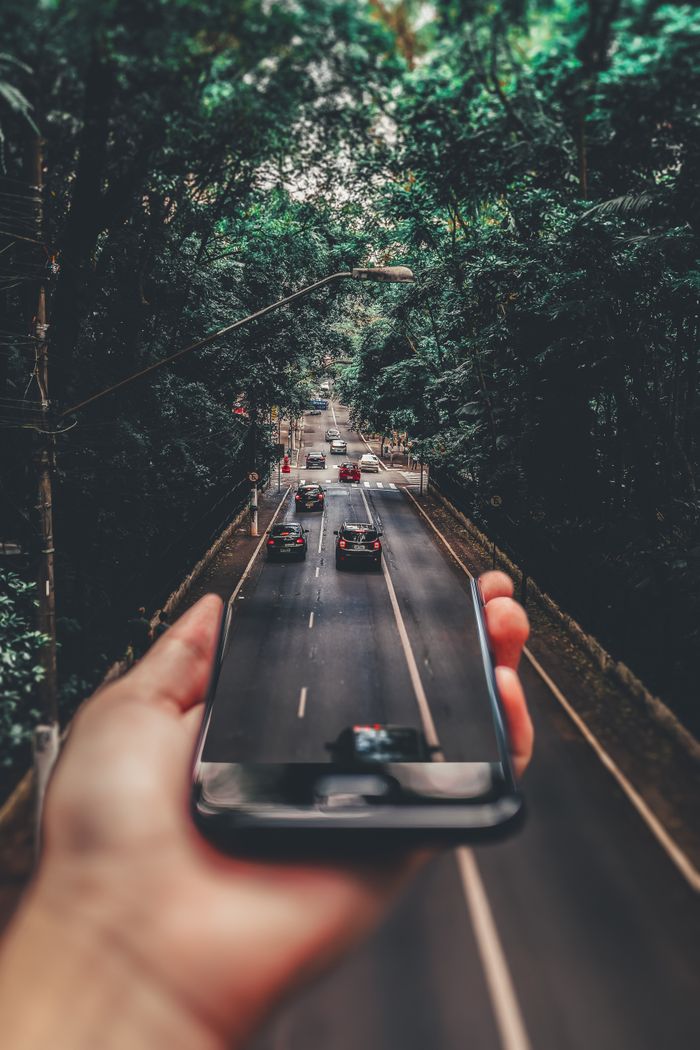 why-choose-us Creative blend of technology and nature with smartphone framing a bustling road through forest.